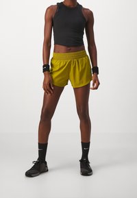 Czarny bezrękawnik typu crop top, jasne żółte sportowe szorty z elastycznym pasem, czarne skarpetki do kostek oraz czarne buty sportowe z akcentami.