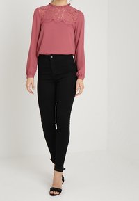 Rosafärgad blus med spetsdetalj, långa ärmar, kombinerad med svarta smala jeans och klacksandaler. Slät tyg, figurnära siluett.