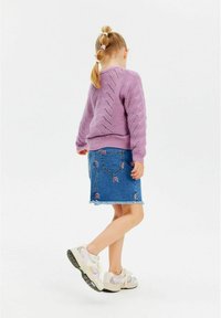 Vijoličen pleteni pulover z teksturiranim vzorcem, v kombinaciji z jeans krilom, ki ima mavrično vezenje in os frayed rob, obut z belimi supergami.
