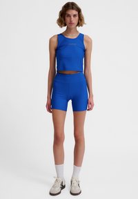 Blue athletic crop top and shorts in a smooth, stretchy fabric. The top features a logo, and the shorts have a high waistband.