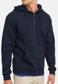 Marineblauwe zip-up hoodie van zachte stof, met een voorzak, trekkoorden en ribbelboorden aan de mouwen en onderkant.