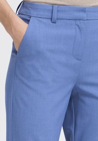 Pantaloni su misura azzurri chiari con una texture liscia, dotati di una tasca laterale e un fronte piatto. La vita è rifinita con cura.