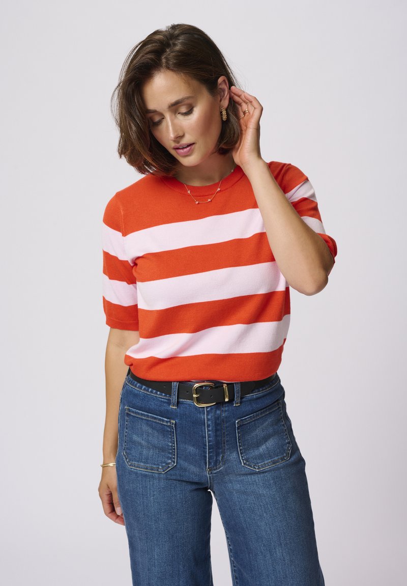 Red and light pink striped knit sweater with short sleeves, round neckline, worn with high-waisted dark denim jeans and a black belt.