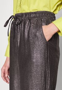 Metalliska mörkgrå byxor med elastisk midja och snöre, med sidofickor och en mjuk, glänsande textur.