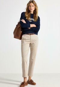 Námořnická mikina s textem "Bonjour Paris", béžové zkrácené kalhoty, hnědý kožený opasek a hnědé šněrovací boty. Hnědá kožená taška.