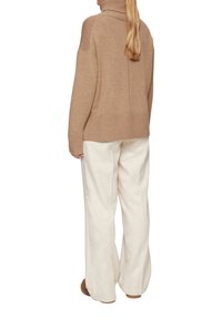 Beige coltrui gemaakt van zachte brei, met ribbeltextuur en een relaxte pasvorm, gecombineerd met roomkleurige wijde broek en lichtbruine laarzen.