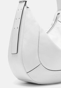 Sac hobo en cuir blanc avec une texture lisse, une forme courbée et une fermeture éclair. Doté d'une longue sangle ajustable avec des perforations.