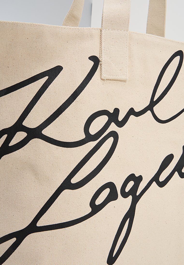 Sac fourre-tout en toile beige avec le texte en cursive noir "Kauli Lagos" et deux poignées en tissu robustes visibles en haut.
