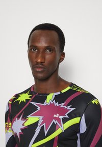 Herren Langarmshirt in Schwarz, mit kräftigen, bunten grafischen Mustern in Lila, Grün und Kastanienbraun. Hergestellt aus einem dehnbaren, glatten Stoff.