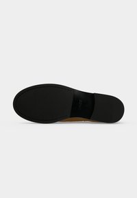 Semelle d'une chaussure habillée noire avec un dessous en cuir lisse et un petit talon, affichant le nom de la marque embossé près de la voûte plantaire.