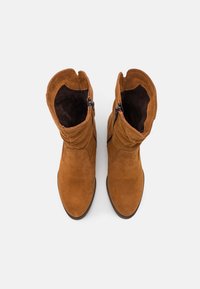 Bottines en suède marron avec un design froncé, dotées de fermetures éclair sur les côtés et d'une texture intérieure douce. Forme classique à bout rond.