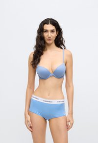Sutien bleu deschis cu cupe netede și bretele ajustabile, asortat cu șorturi hipster bleu deschis, având o bandă albă Calvin Klein în talie.