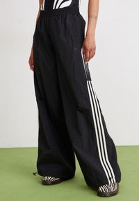 Svarte vide bukser laget av lett materiale, med hvite vertikale striper og elastisk midje. Akkuratert med mønstrede fottøy.