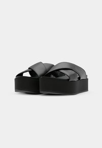 Sandali platform neri con larghe cinghie incrociate realizzate in materiale liscio e una base spessa e solida. Design minimalista senza hardware visibile.