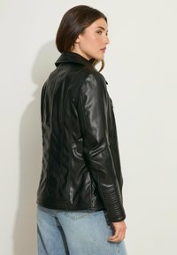 Giubbotto in pelle nera con colletto, caratterizzato da dettagli a coste sulle maniche e una texture liscia. Indossato con jeans in denim blu.