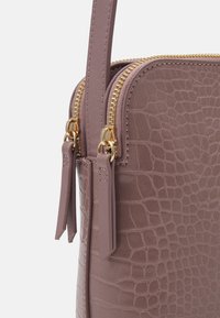 Mauve keinonahkahandbag, jossa on krokotiilinjälki, kahdella kultaisella vetoketjulla ja yhteensopivalla hihnalla.