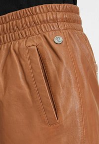 Bruine leren shorts met een elastische tailleband, zijzakken en een metalen accent met merknaam. De textuur is glad en licht glanzend.