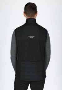 Schwarze Weste mit einem gesteppte unteren Teil und glattem oberen Stoff. Sie verfügt über einen hohen Kragen und ein "Swedemount"-Logo auf der Rückseite.