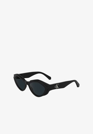 Ochelari de soare negri în stil cat-eye, cu o finisare lucioasă, lentile închise la culoare și un logo „cK” pe braț. Design unghiular și rame groase.
