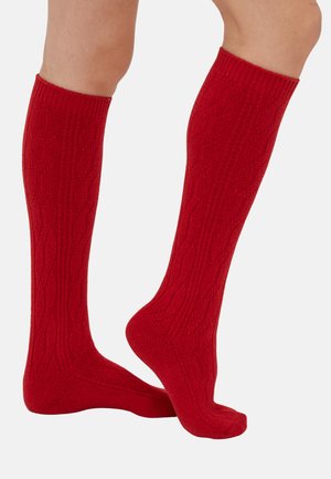 Chaussettes rouges jusqu'aux genoux en tissu tricoté texturé, présentant un motif en zigzag subtil et des poignets côtelés pour un ajustement sécurisé.