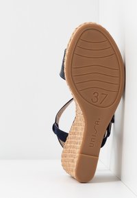 Sandale compensée avec talon en paille tressée, lanières bleu marine et semelle en caoutchouc beige indiquant la pointure 37 et le logo de la marque "Unisa".