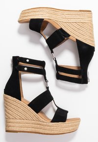 Czarne zamszowe sandały na koturnie z plecionymi detalami z juty, regulowane paski oraz zaokrąglony przód. Gładkie wykończenie wewnętrzne i subtelne akcenty metalowe.