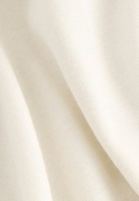 Gros plan d'un tissu doux couleur crème avec une texture fine tricotée et des plis délicats créant des ombres subtiles.