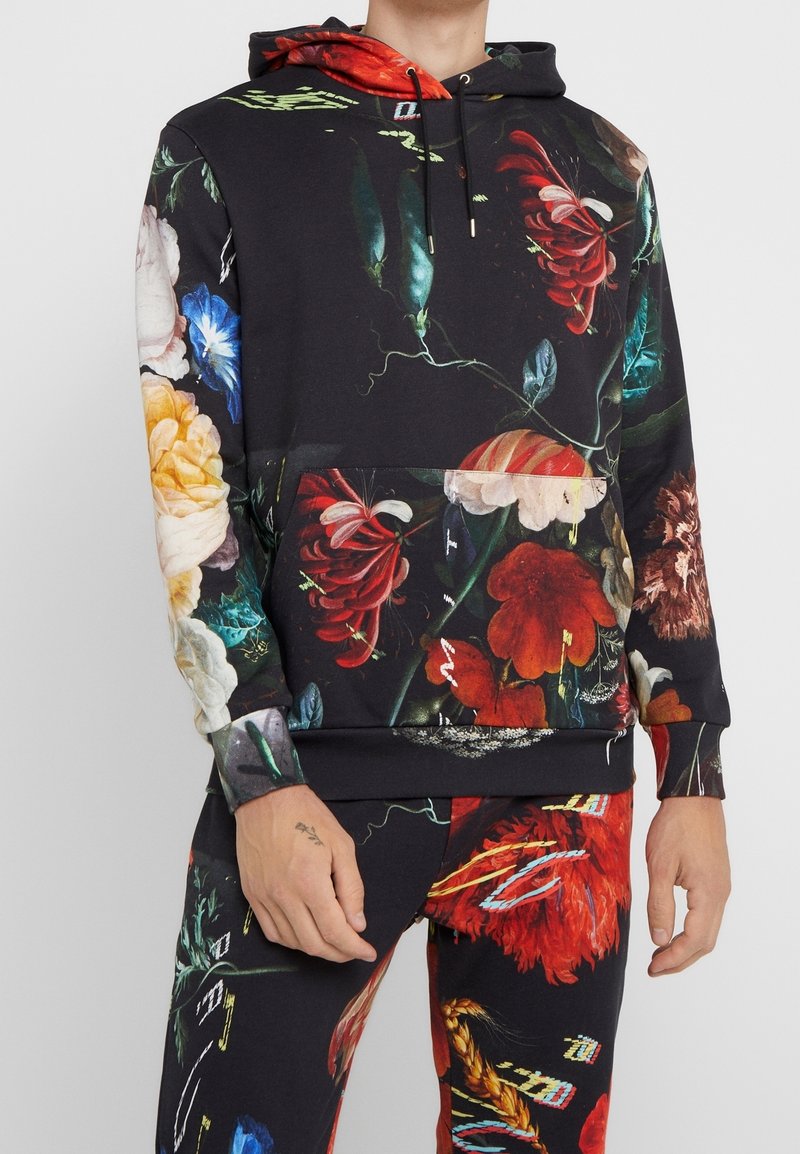 Hoodie i svart tyg med ett övergripande blommönster i livfulla färger. Inkluderar en framtill placerad ficka och ribbade ärmslut.