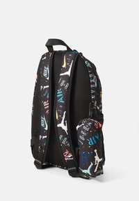 Sac à dos noir avec un motif graphique multicolore comprenant des logos et des silhouettes. Il dispose d'un rembourrage en mesh, de bretelles ajustables et d'une poche latérale.