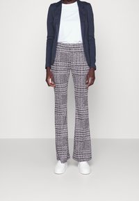 Gray and white patterned flared pants with a textured finish, paired with a plain white shirt and a navy blazer, worn with white sneakers.