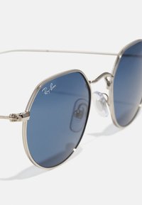 Ray-Ban akiniai su mėlyna šviesą blokuojančia danga, sidabriniu metaliniu rėmu ir tekstūruotais akcentais. Yra nosies pagalvėlės ir unikali forma.