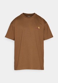 Camiseta de algodón marrón con cuello redondo, mangas cortas y un pequeño logo en el pecho en amarillo y rojo. Textura suave, diseño informal.