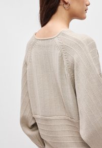 Pulover tricotat bej, cu nervuri verticale, mâneci largi și decolteu tip barcă. Caracteristici includ un material texturat și o croială lejeră.