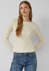 Długi rękaw, jasnobeżowy top o delikatnej prążkowanej fakturze, z okrągłym dekoltem i luźnym krojem, w połączeniu z wysokim stanem niebieskich dżinsów.