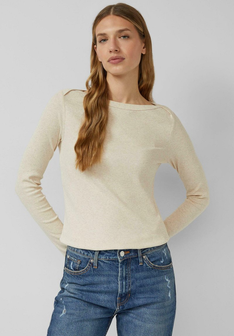 Długi rękaw, jasnobeżowy top o delikatnej prążkowanej fakturze, z okrągłym dekoltem i luźnym krojem, w połączeniu z wysokim stanem niebieskich dżinsów.