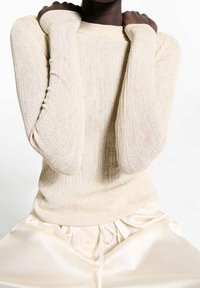Beige geripptes Strickpullover mit langen Ärmeln und Daumenlöchern, kombiniert mit weichen, cremefarbenen Seidenhosen. Glatte Textur, taillierte Passform.