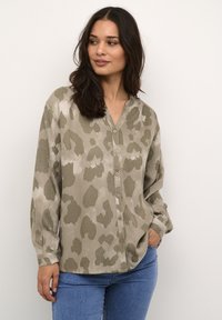 Camisa de patrón verde y beige con escote en V, manga larga y botones en la parte frontal. Tela suave y texturizada, corte relajado.