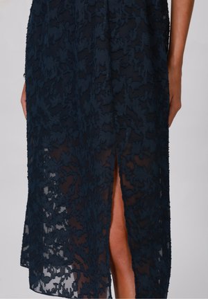 Navy blue floral lace skirt with a front slit showing part of a leg and two arms positioned at the sides.