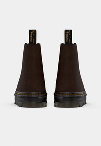 Bottines en cuir marron avec des côtés élastiques, coutures jaunes contrastantes, semelle en caoutchouc noir épaisse et languettes à l'arrière.