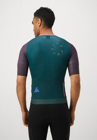 T-shirt de sport à manches courtes en turquoise et violet avec des panneaux texturés. Présente un logo circulaire au dos, une poche zippée sur le côté et des accents contrastés.