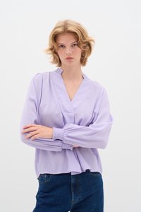 Blusa lavanda chiara con maniche lunghe, scollatura a V, dettagli del colletto plissettati e polsini elasticizzati, abbinata a jeans di denim blu scuro.