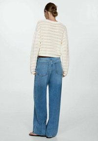 Pull crème en maille crochet avec manches longues, associé à un jean large bleu clair avec poches arrière. Texture lisse, coupe décontractée.