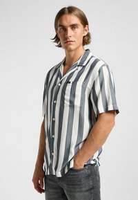 Chemise à manches courtes rayée bleu marine et blanche, avec un col boutonné, une poche poitrine simple et une texture de tissu léger.