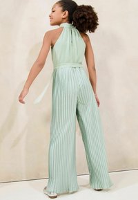Combinaison plissée vert menthe avec un col halter et une ceinture à nouer, présentant des jambes larges et un tissu lisse et texturé.