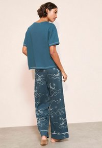 Tirkīza kokvilnas mājas apģērba komplekts, kas sastāv no īsām piedurknēm un plašām biksēm ar debesu motīvu, kas attēlo mākoņus un mēnešus. Kontrasta šuvju akcenti.