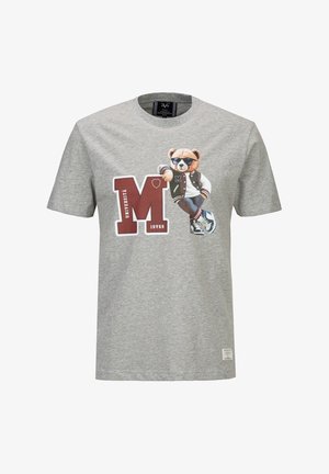 T-shirt gris avec un grand "M" rouge et un ours portant des lunettes de soleil, une veste universitaire, un jean et des baskets, appuyé sur le "M" à l'avant.