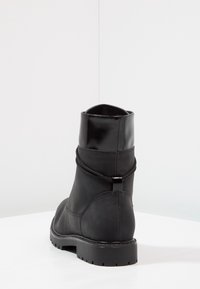 Svart stövel med matt läderfinish, rundad tå och en slät glansig ovansida. Har en dragring, texturerad sida och en robust sula.