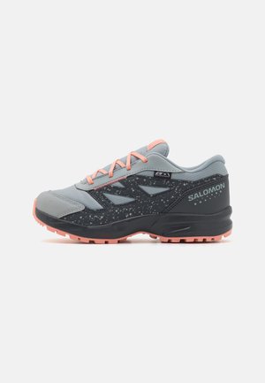 Zapatilla de running gris y negra con detalles en rosa, parte superior de malla y sintético, suela texturizada con patrones de agarre, y puntera reforzada.