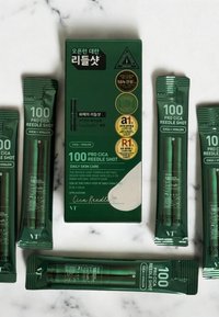 Grön förpackning med "100 Pro Cica Reedle Shot", som innehåller fem rör och en låda, alla märkta med text. Texten beskriver produktens användning och ingredienser.