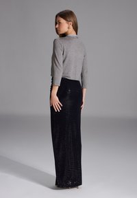 Maglione grigio corto con maniche a tre quarti abbinato a una gonna nera lunga di paillettes con finitura testurizzata e arricciatura laterale.